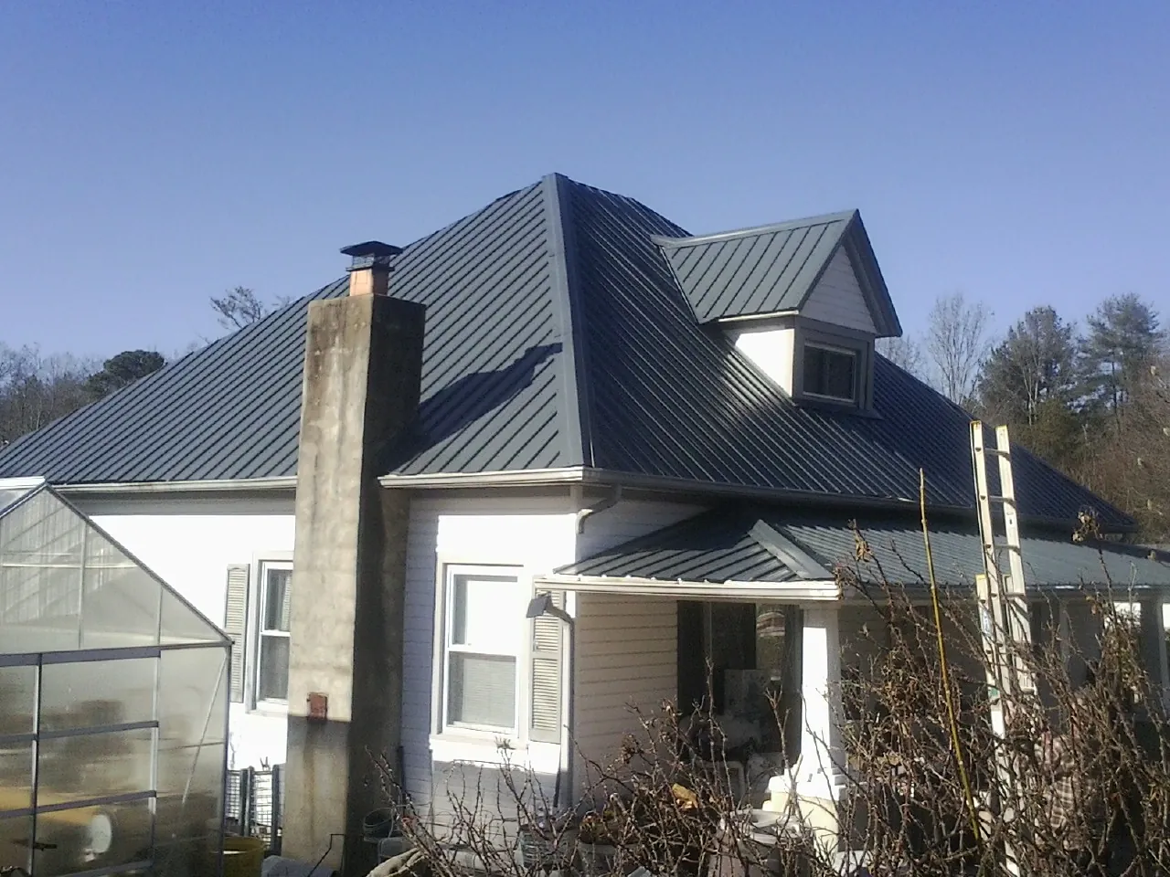 Dark blue standing seam metal roof on a white farmhouse with dormer — Slate & Tile Roof Repair by Roofing Brothers in Cheraw