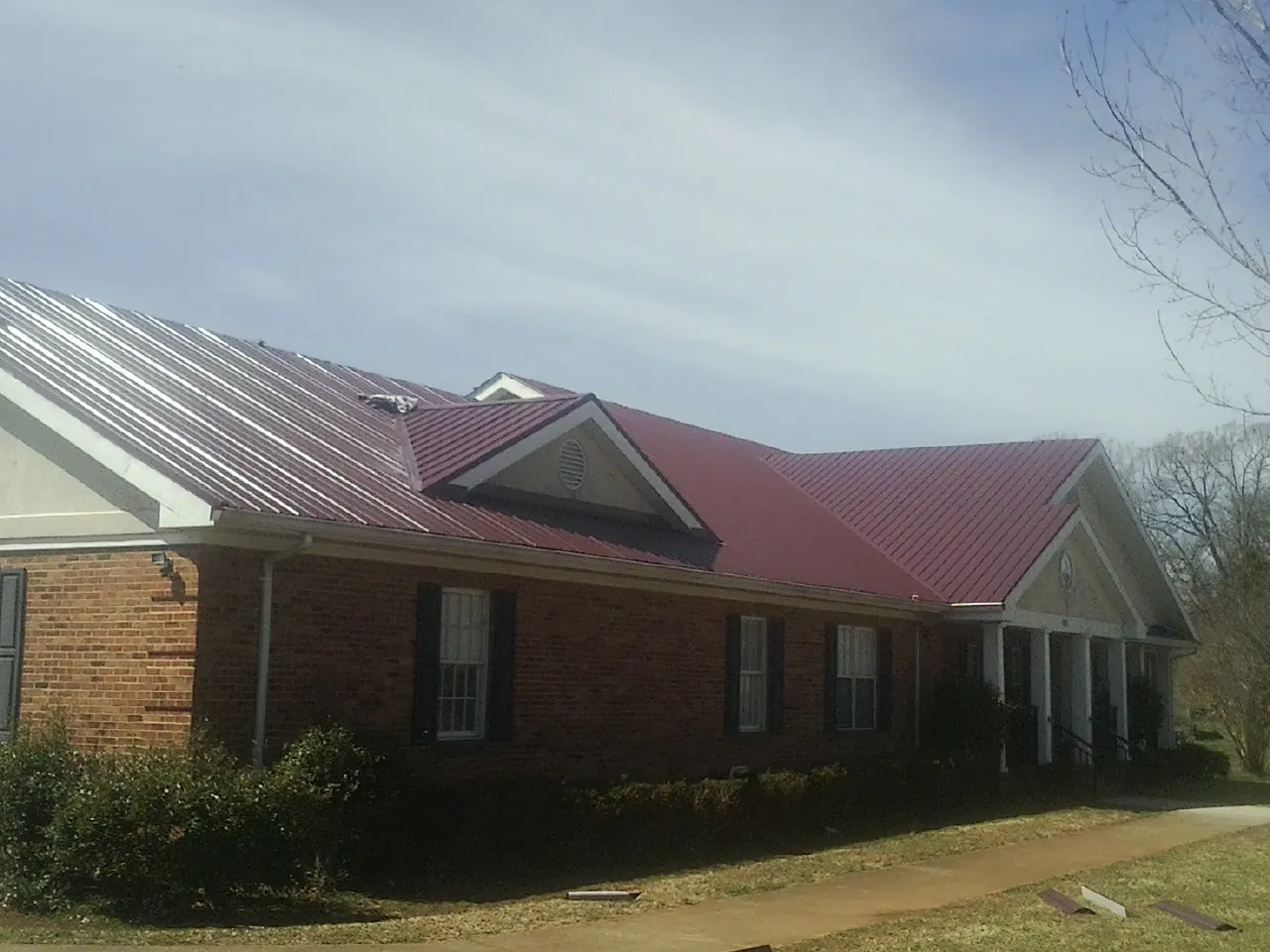 Red metal roof with gabled entries on a long brick building, from a Hail Damage Roof Repair job in Cheraw
