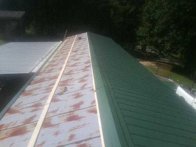 Old rusted panels beside newly installed green metal roofing — Wind Damage Roof Repair by Roofing Brothers in Cheraw