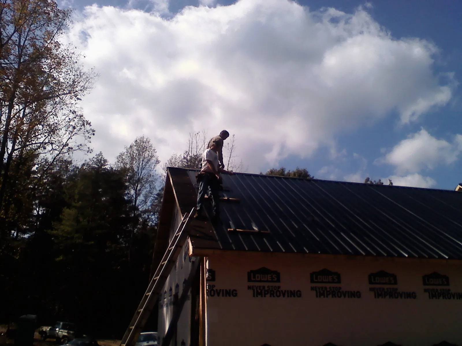 Roofer fastening dark metal panels high against a cloudy sky, from a Roof Inspection job in Cheraw