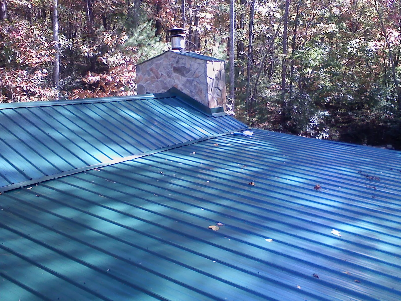 New green metal roof and stone chimney surrounded by autumn woods in Cheraw