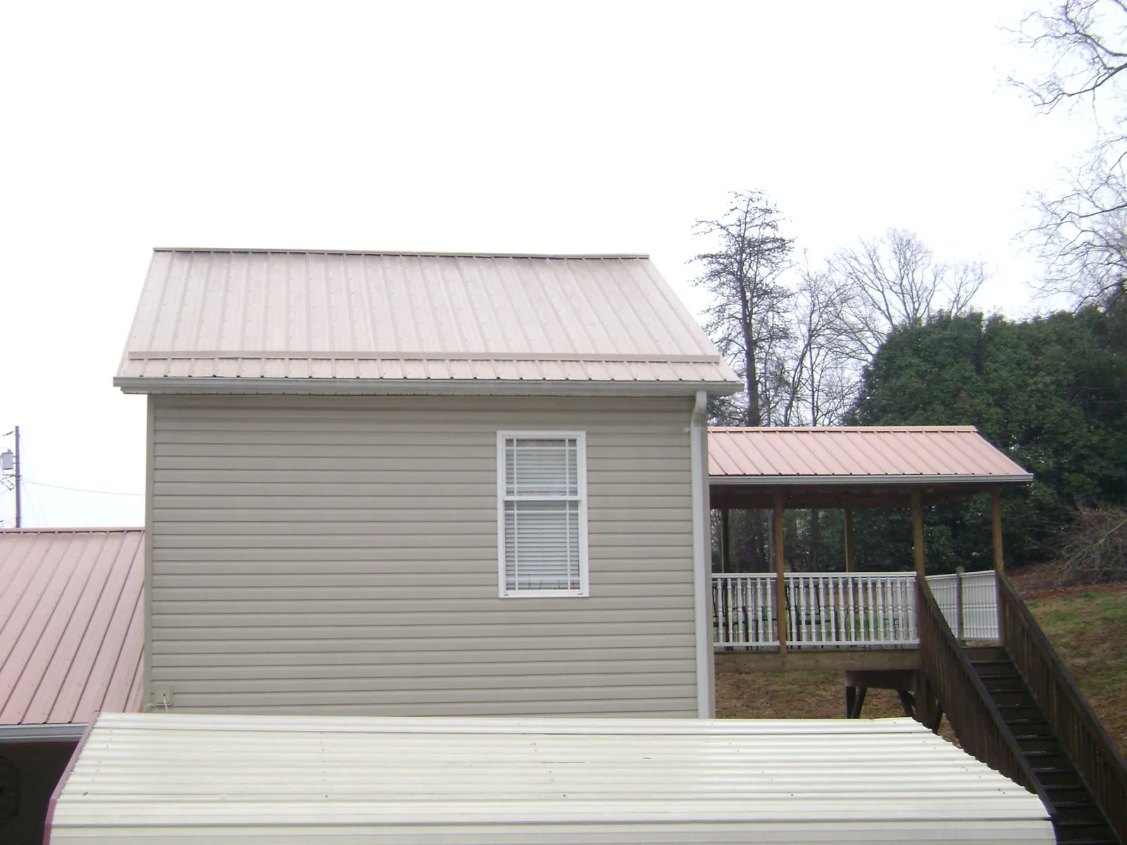Tan metal roofs on a two story addition and attached porch, from a Roof Replacement job in Cheraw